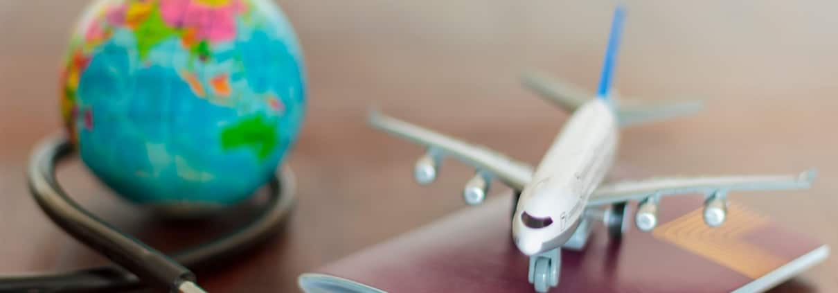 Close up of a miniature plane, globe, passport and stethoscope