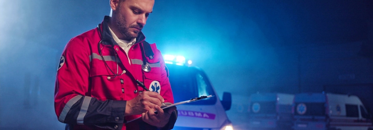 Male EMS professional writing on a clipboard in front of an ambulance